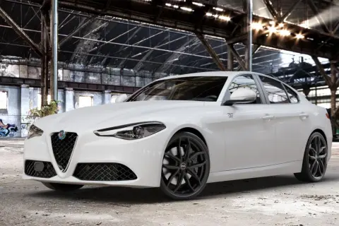 Biała Alfa Romeo Giulia Veloce z czarnymi felgami stoi w opuszczonej hali przemysłowej, gdzie światło przebija się przez dach.