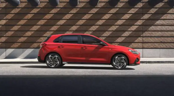 Czerwony Hyundai i30 hatchback stoi na tle ceglanej ściany z ciekawymi cieniami.