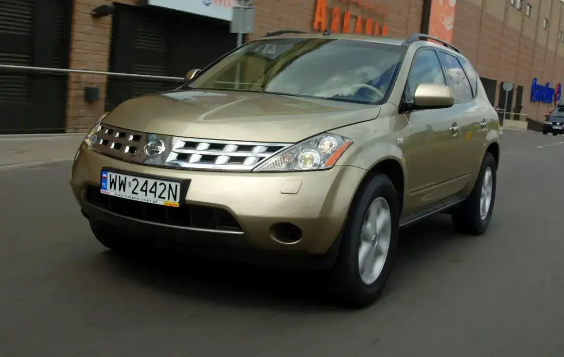 Złoty Nissan Murano 3.5 V6 w ruchu miejskim. Elegancki SUV z charakterystycznym grillem i reflektorami.