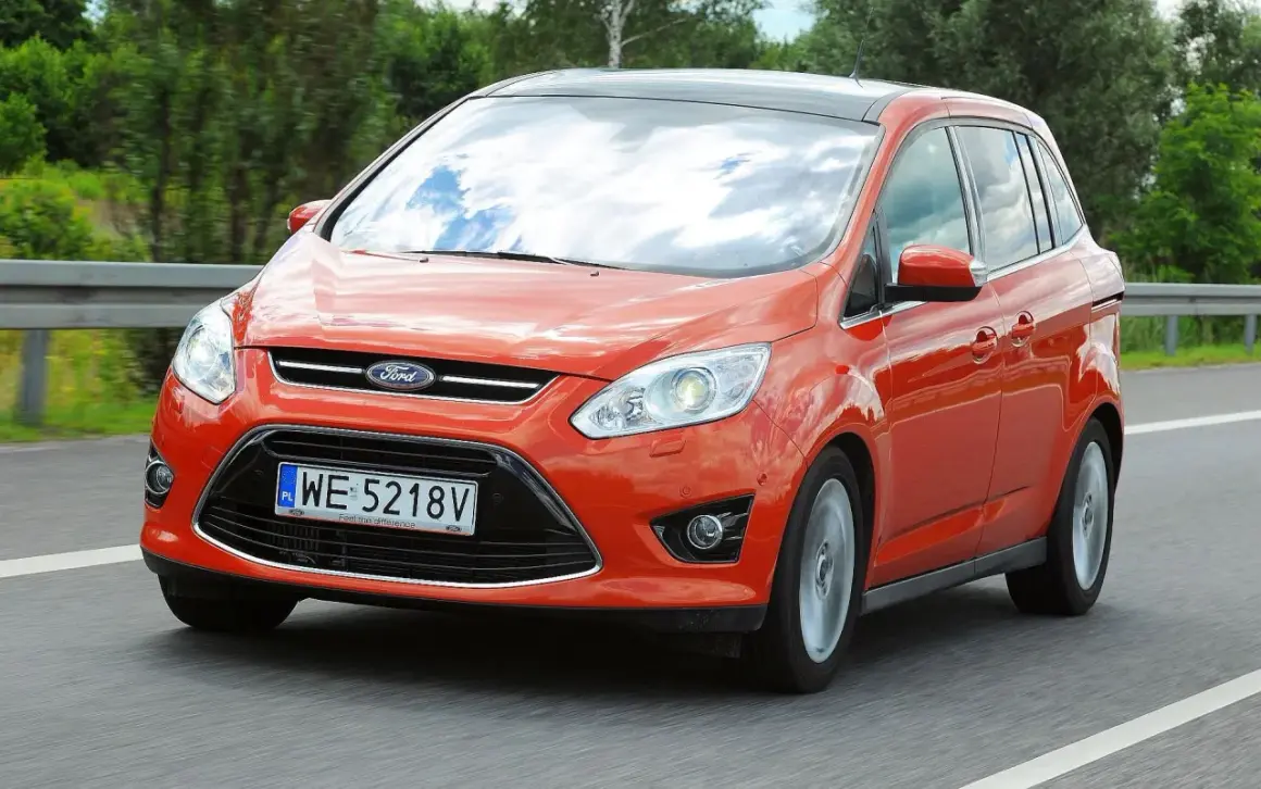 Pomarańczowy Ford C-Max 1.6 TDCI w ruchu drogowym, z widocznym niebem odbijającym się w szybach.