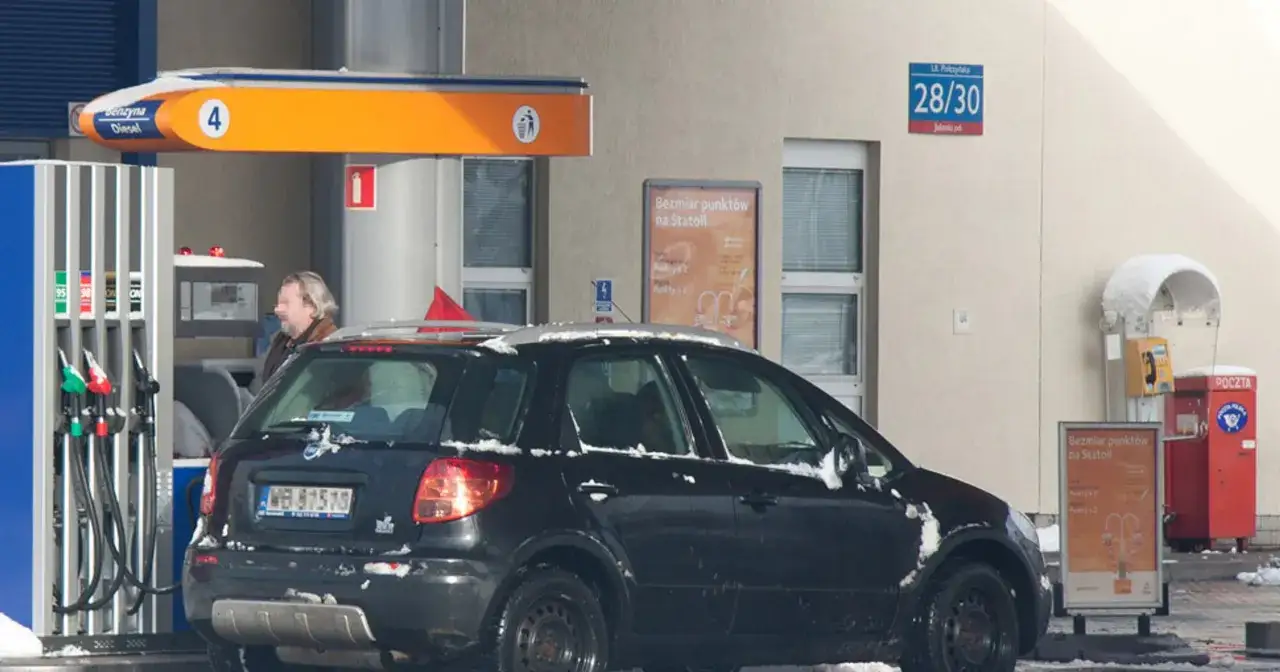 Czarny samochód na stacji benzynowej, tankowanie verva diesel. Śnieg na dachu auta i dystrybutorze.