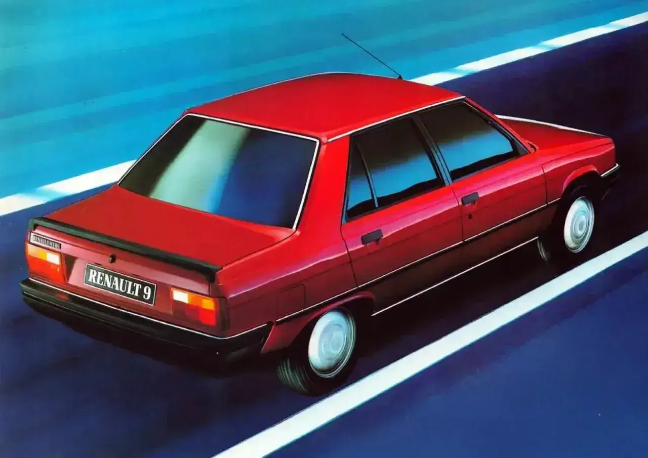 Czerwony Renault 9 sunie po drodze, odbijając niebieskie niebo w szybach. Klasyk z lat 80.