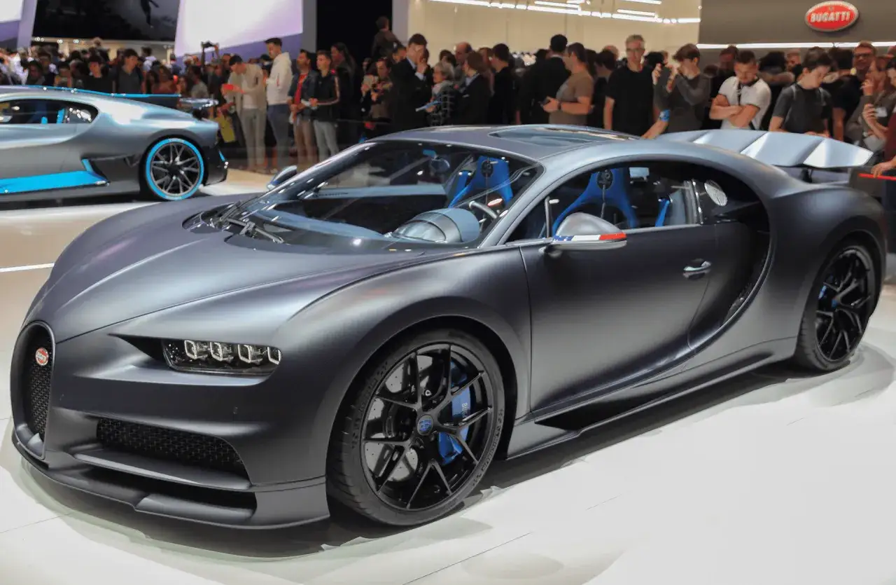 Szary Bugatti Chiron Super Sport z niebieskimi akcentami, prezentowany na wystawie samochodowej, przyciąga uwagę tłumu.
